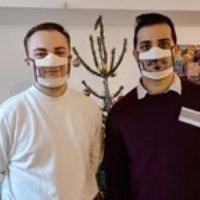 Photo de deux jeunes hommes portant des Masques Sourire devant un sapin de Noël